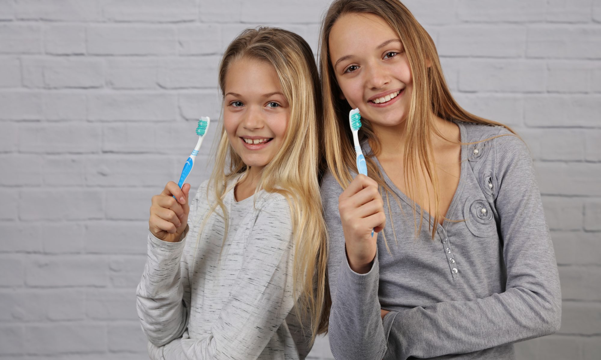 Portrait of two beautiful girls kids with perfect smile holding toothbrushes. Child dental care, oral hygiene concept